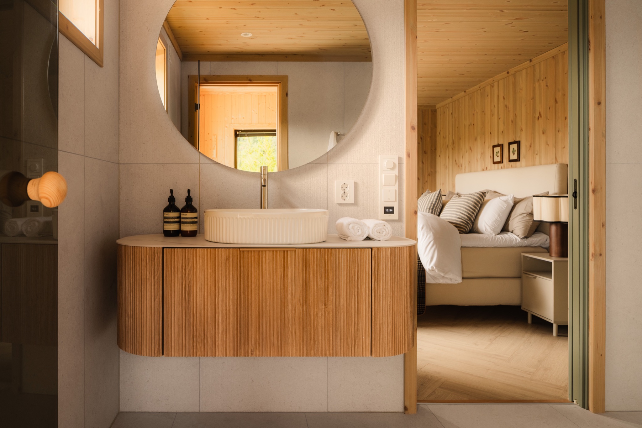 En-suite badkamer met ronde spiegel en wastafel, met zicht op de master bedroom